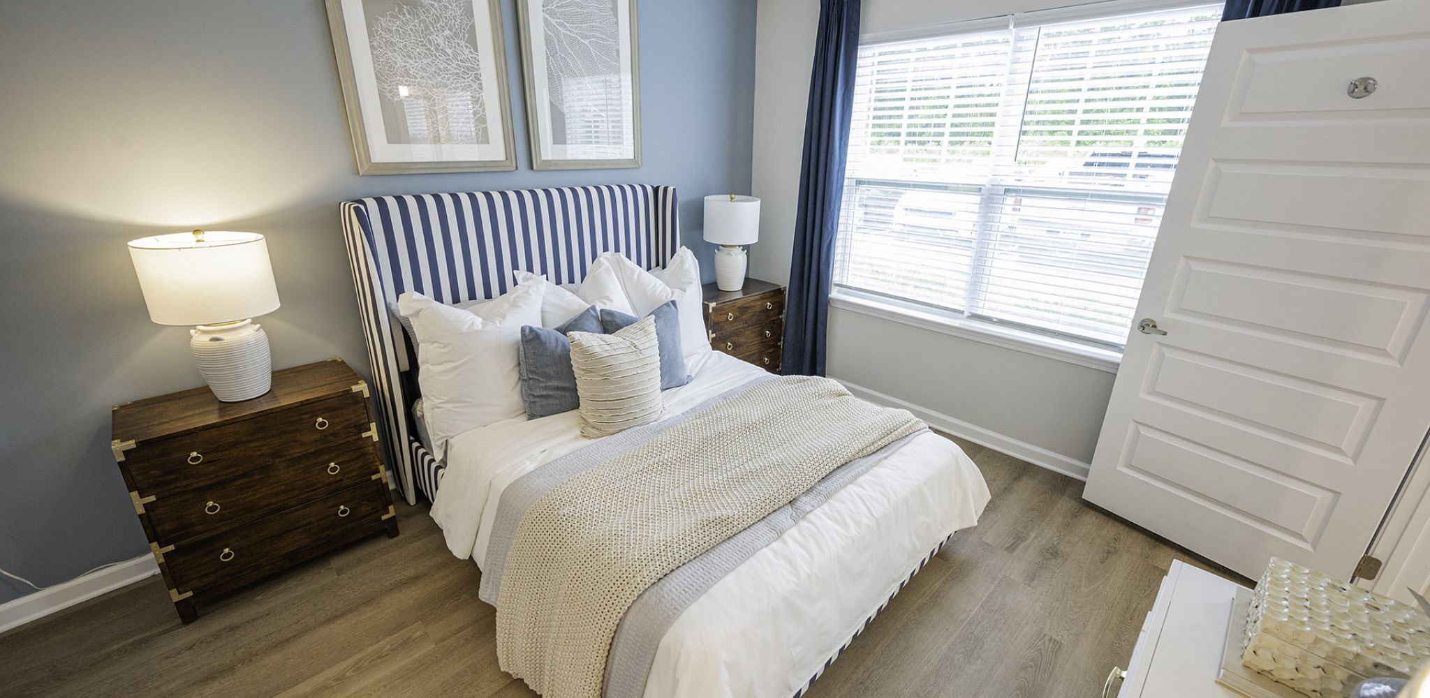 Hawthorne Waterside elegantly furnished bedroom with a striped headboard, chic bedside tables, and framed art above.