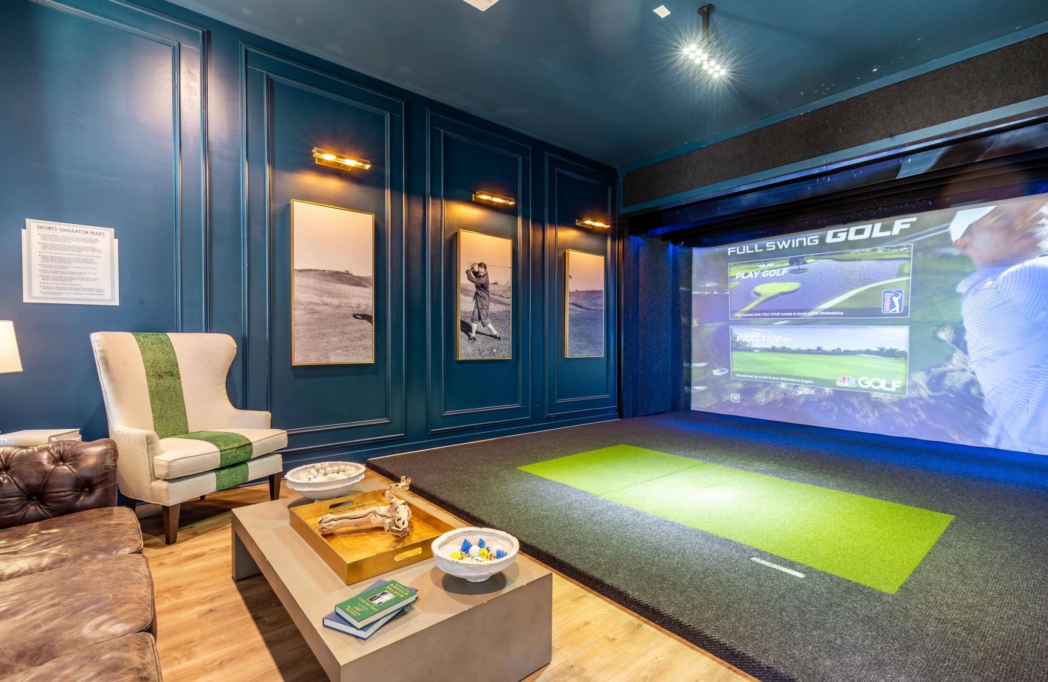 Hawthorne Waterside luxurious indoor golf simulator room with a leather sofa, accent chair, and framed vintage golf photos.