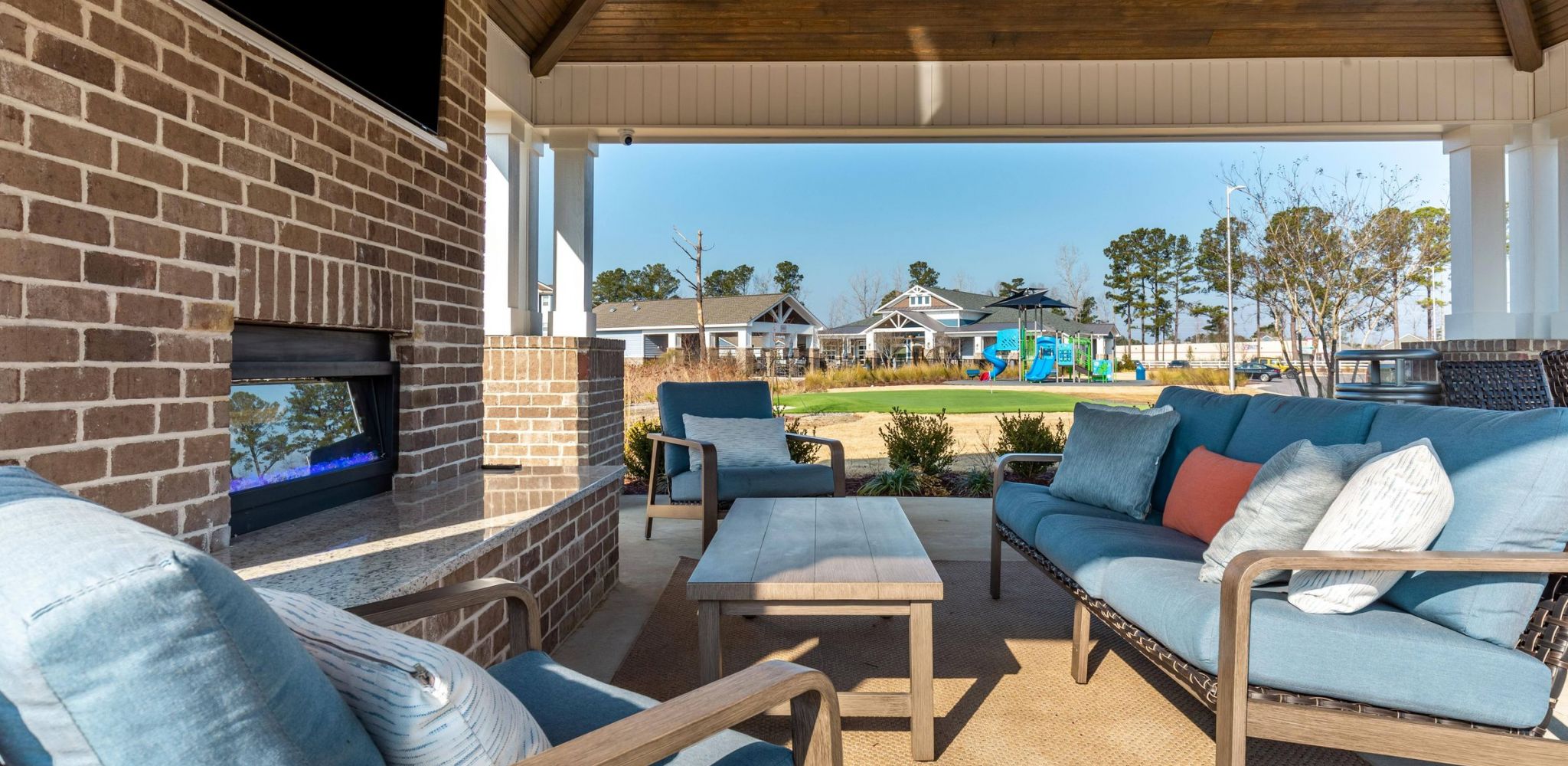 Hawthorne Waterside outdoor covered patio area with a cozy fireplace, comfortable seating, and a clear view of the playground.